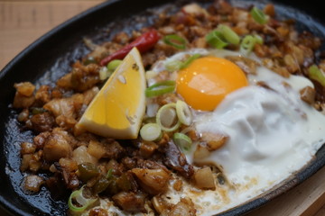 Pork sisig sizzling mince pork Filipino food with raw egg cooking hot on clay pot tray with lemon slice and fresh red chilies Asian cuisine tasty food with pepper on plate 