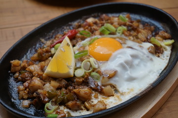 Pork sisig sizzling mince pork Filipino food with raw egg cooking hot on clay pot tray with lemon slice and fresh red chilies Asian cuisine tasty food with pepper on plate 