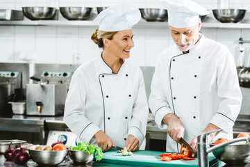 female and male chefs in uniform cutting ingredients while cooking in restaurant kitchen