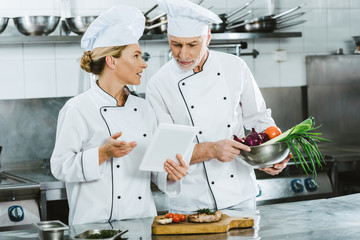 female and male chefs in uniforms using digital tablet during cooking in restaurant kitchen