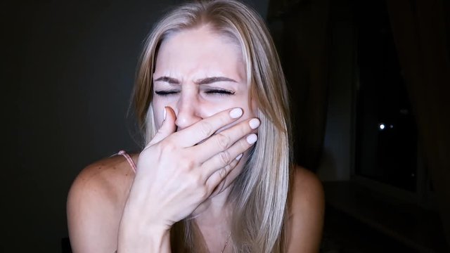 beautiful young blond woman with bright blue eyes yawns during a boring conversation, listens to the interlocutor, smiles and nods, uninteresting conversation, close-up portrait against a dark backgro