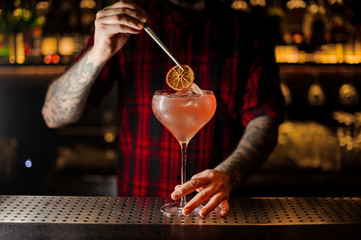 Barman decorating sweet alcoholic cocktail with a slice of orange