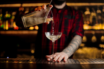 Bartender pouring alcoholic cocktail into an elegant glass