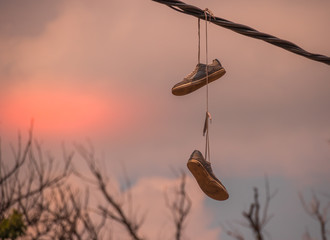 A pair of sneakers hanging from an overhead power line isolated against the skyline image with copy...