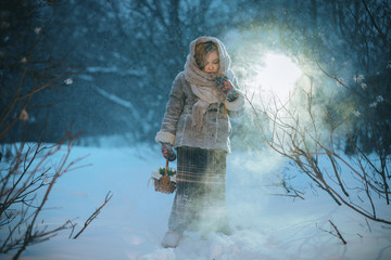little child girl with a basket goes and looks for the first flowers under the snow in the forest...