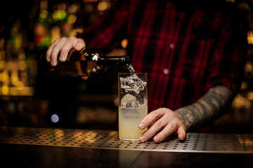 Mixologist pouring alcoholic drink from bottle into a cocktail glass with juice and ice