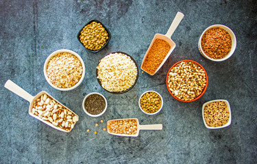 Cereals and legumes in the range. Peas, beans, lentils, rice, quinoa, chia seeds, oatmeal, in small cups and scoops on a dark stone background, culinary background, background about products