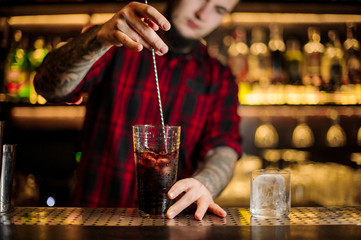 Barman stirring fresh strong alcoholic cocktail in a big glass
