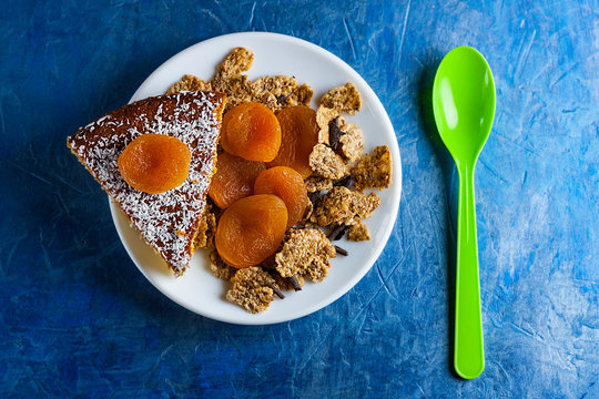 PLATO CON BIZCOCHO DE COCO, OREJONES DULCES Y CEREALES INTEGRALES CON CUCHARA VERDE