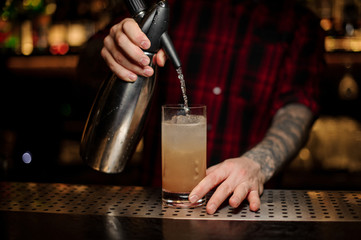Barman adding soda water to an alcoholic orange cocktail