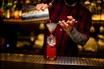 Fototapeta na wymiar Barman pouring red sweet juicy drink into a cocktail glass