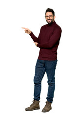Full-length shot of Handsome man with glasses pointing finger to the side in lateral position on isolated white background