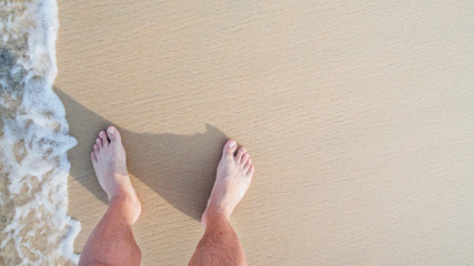 Closeup of a man's bare feet stand at wet on the beach , with a wave's edge foaming gently beneath them. Vacation on ocean beach, foot on sea sand. Leave empty copy space Enter the text above.