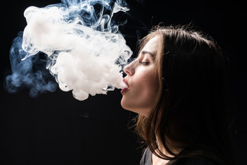 Young woman smoking electronic cigarette vaping a cloud of smoke isolated on dark background