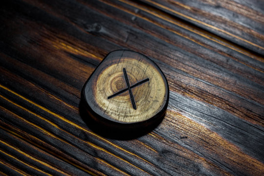 Rune Gyfu (Gebo) carved from wood on a wooden background - Elder Futhark
