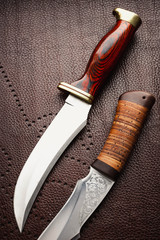 Two hunting knifes on brown background.