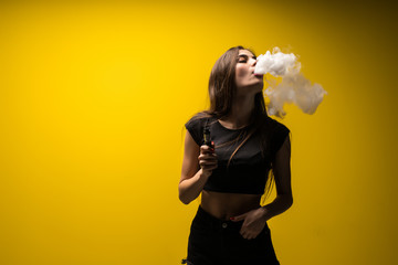 Attractive glamour woman standing and vaping on yellow background