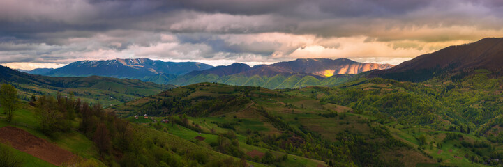 Fototapeta na wymiar panorama of a wonderful countryside in mountains. rural fields on rolling hills. village in the distant valley. beautiful landscape in spring at sunset