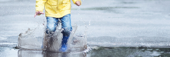 A wet child is jumping in a puddle. Fun on the street. Tempering in summer