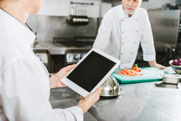 partial view of female chef using digital tablet with blank screen in restaurant kitchen