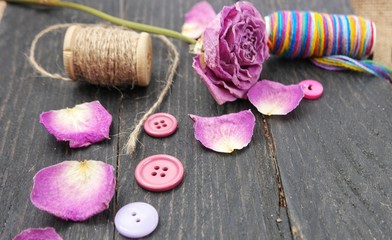 Decorative composition of purple buttons, threads and dry rose on a wooden board