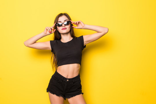 Portrait of smiling young woman in summer clothes and sunglasses isolated over yellow background