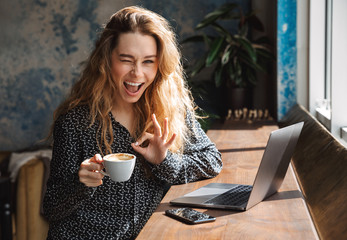 Young pretty woman sitting in cafe indoors using laptop computer drinking coffee.