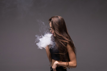 Young beauty woman wearing in sunglasses smoking vape on gray background