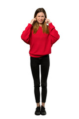 A full-length shot of a Young woman with red sweater frustrated and covering ears with hands over isolated white background