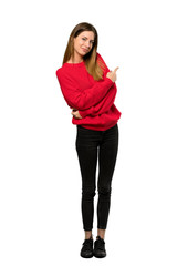 A full-length shot of a Young woman with red sweater pointing back over isolated white background