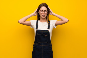 Woman over yellow wall frustrated and takes hands on head