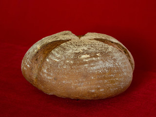 Bread loaf with cuts from spelt prepared in an electrooven on a red background.