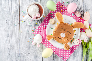Funny easter breakfast food, kids pancake in form of bunny rabbit, with hot chocolate, top view wooden background copy space