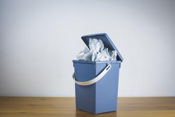 Gray trash can filled with crumpled paper