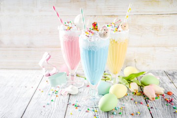Funny easter food, ideas recipes for children Easter party, colorful blue yellow pink milkshakes with sugar sprinkles, wooden background with Easter egg and bunny rabbit decoration, copy space