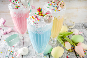Funny easter food, ideas recipes for children Easter party, colorful blue yellow pink milkshakes with sugar sprinkles, wooden background with Easter egg and bunny rabbit decoration, copy space