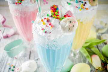 Funny easter food, ideas recipes for children Easter party, colorful blue yellow pink milkshakes with sugar sprinkles, wooden background with Easter egg and bunny rabbit decoration, copy space