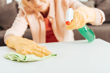Obraz na płótnie Canvas Partial view of woman in yellow rubber gloves cleaning table surface with rag and spray