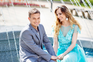 Pleasant walk. Delighted positive couple sitting near the fountain while having a walk together. Happy married couple enjoying fountains while having a walk in the neighborhood