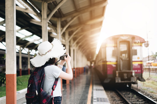 Travel concept. Attractive young woman hand holding camera and travel bag at the train station in Chiang Mai, Thailand. Young passenger girl take pictures with camera in her hand