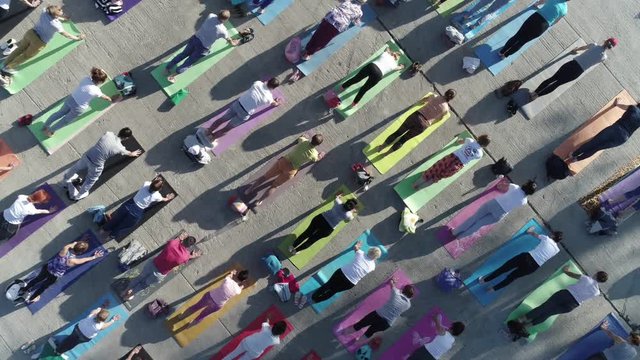 aerial view on big group of adults attending a yoga class outside in park