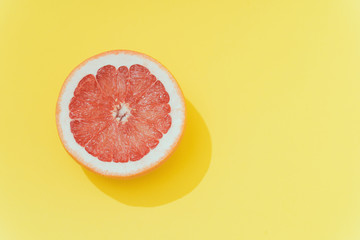 Red grapefruit slice on pastel yellow background. Minimal summer concept.