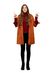 Full-length shot of Young woman with coat pointing with the index finger a great idea on isolated white background