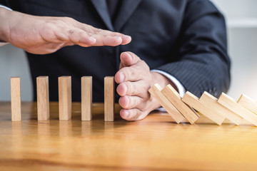Wooden game strategy, Businessman hand stopping falling wooden dominoes effect from continuous...