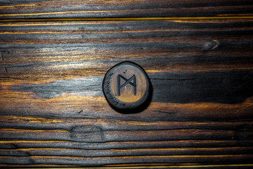 Rune Mannaz (Mann) carved from wood on a wooden background - Elder Futhark