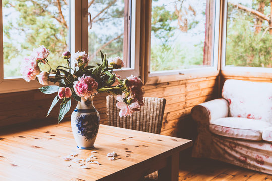 A cozy terrace with furniture - a sofa, peonies in a vase on the table and wicker chairs with a view of the forest. Tinted image