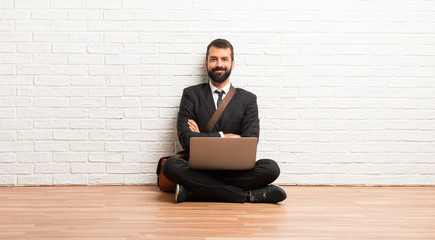 Businessman with his laptop sitting on the floor keeping the arms crossed in frontal position