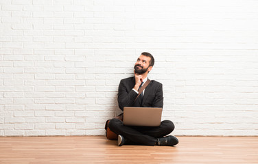 Businessman with his laptop sitting on the floor standing and thinking an idea while looking up