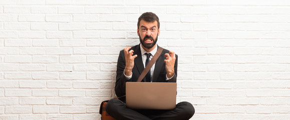 Businessman with his laptop sitting on the floor annoyed angry in furious gesture