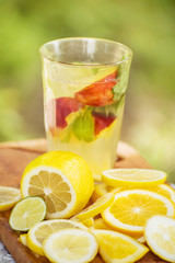 Fruit orange lemonade in a glass and various citrus fruits on a natural background in the garden.